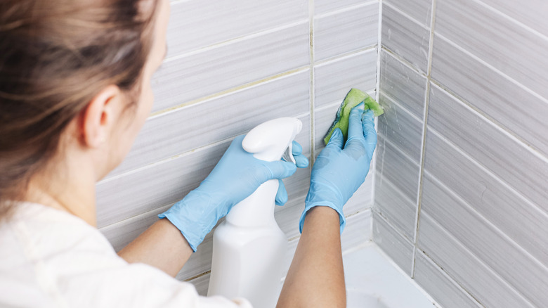 woman cleaning grout in bathroom with spray cleaner and a sponge