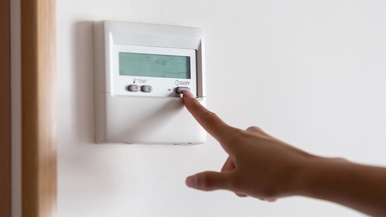 A hand turning off the wall thermostat at home