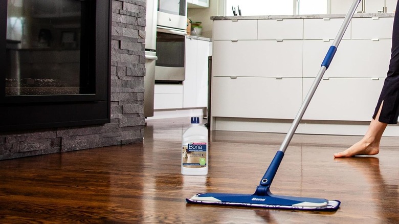 A barefoot person uses a large mop to apply Bona Hardwood Floor Polish to kitchen floors