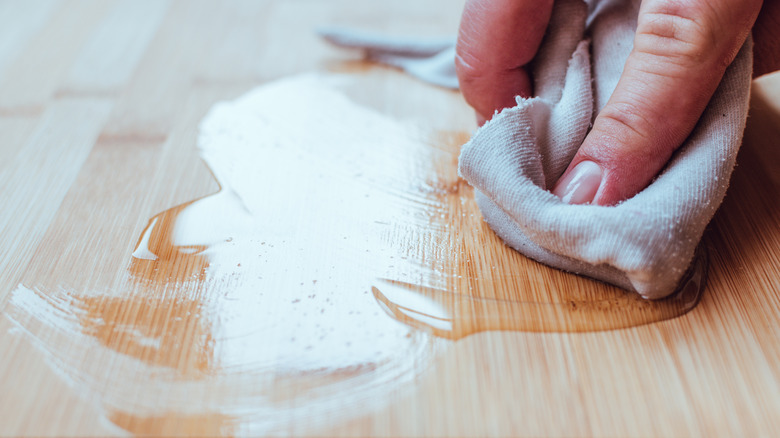 A person uses a clean microfiber cloth to apply beeswax to a hardwood floor