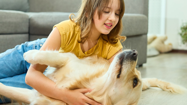 Girl in yellow shirt and jeans laying with a golden retriever