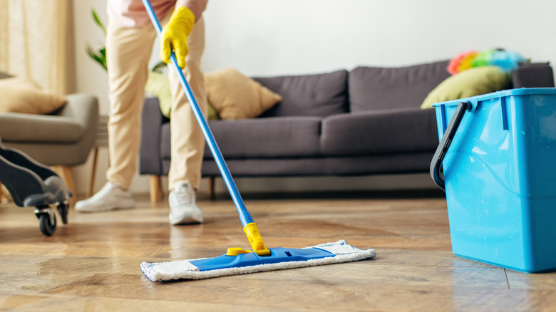 Person cleaning living room floor with a blue cloth mop and bucket
