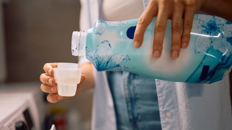 Someone with a fabric softener bottle pouring it into the cup to pour into a laundry machine