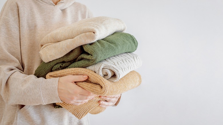 woman holding stack of sweaters