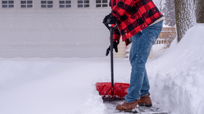 Person in red flannel coat shoveling snow on driveway