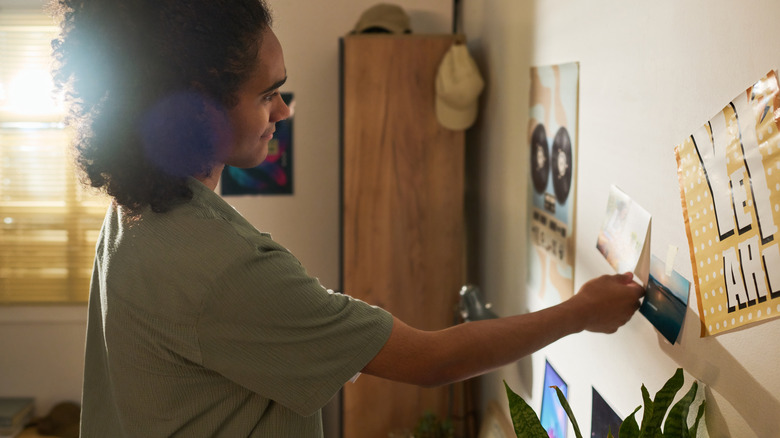 Young man hanging up picture on collage wall