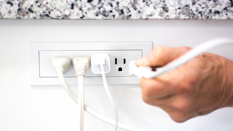A light-skinned hand plugs another cord into a side-mounted outlet.