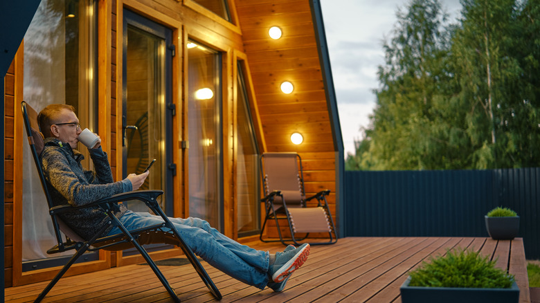 A man sits on his deck lounger in the evening, with yellowish outdoor lights turned on