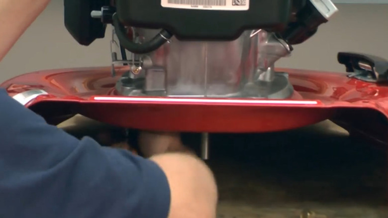 Someone removing the bolts from a mower deck