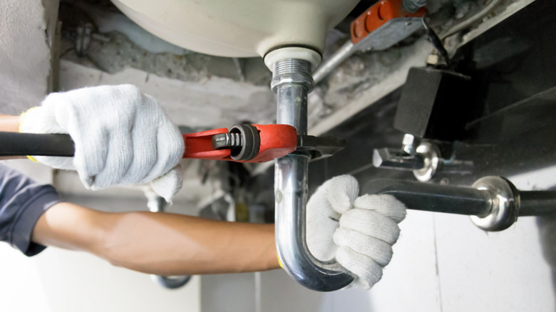 Person disconnecting the P-trap pipe with a wrench