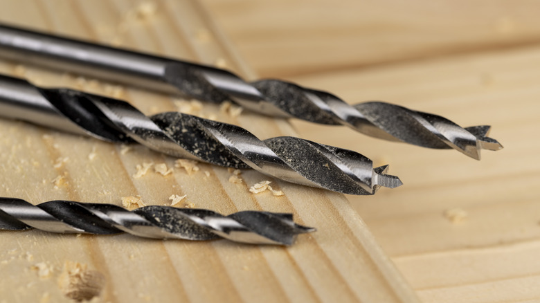 Metal drill bits with saw dust after drilling holes into a pine board.
