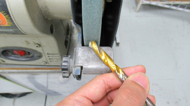 A hand sharpening a drill bit on a bench grinder.