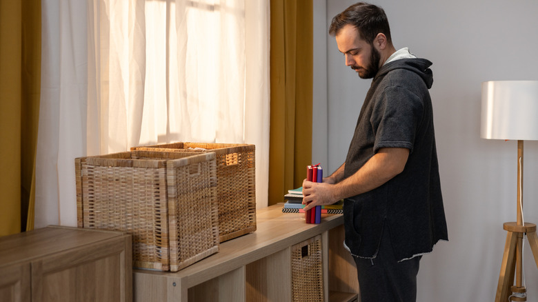 Man sorting books and organizing them in wicker baskets on shelves.