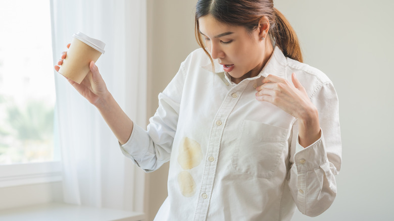 Woman looking at coffee stains on her shirt while holding a go-to cup in hand