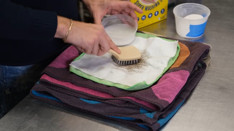 Hands using a thick brush to work in laundry boosters on mud stains