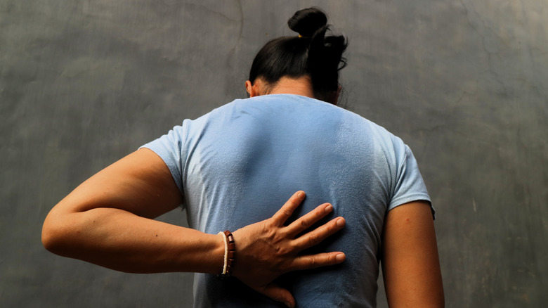 Woman touching her back, with sweat staining on back of tee shirt