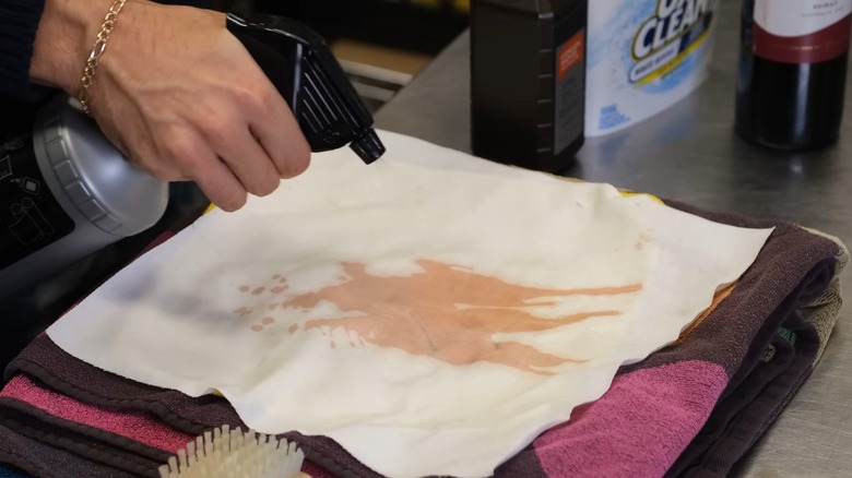 Man spraying a solvent on a dark stain on a white cloth
