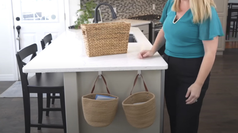 A woman standing beside kitchen table with two hanging baskets attached to it to keep countertops clear