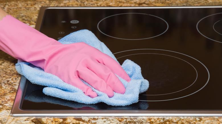 Pink gloved hand wiping induction cooktop with a microfiber cloth