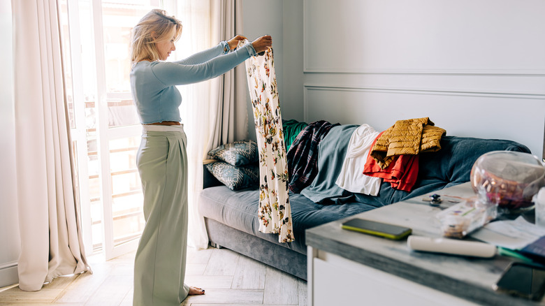Woman holding up clothes from pile on couch