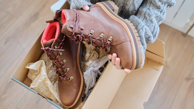 Hands holding brown boots over a cardboard box