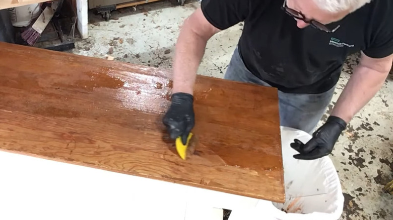 Man using glass from a picture frame to scrape stripped paint