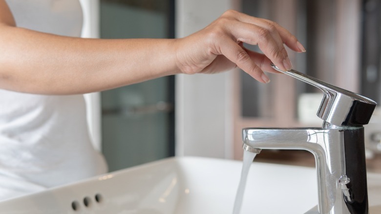 Woman's hand turning off faucet