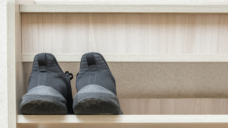Pair of black tennis shoes on shelf of a wooden shoe rack