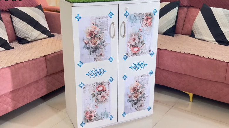 White decoupaged shoe rack with doors on a tile floor next to pink couch