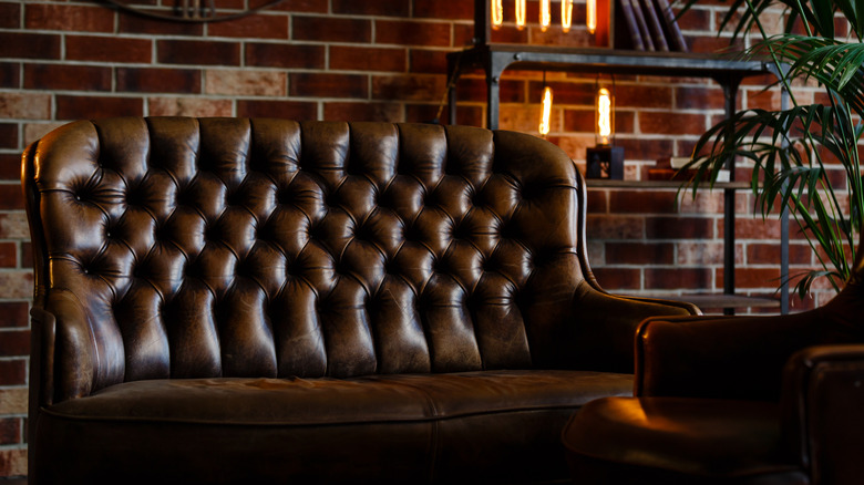 Tufted dark leather chair against brick with natural light