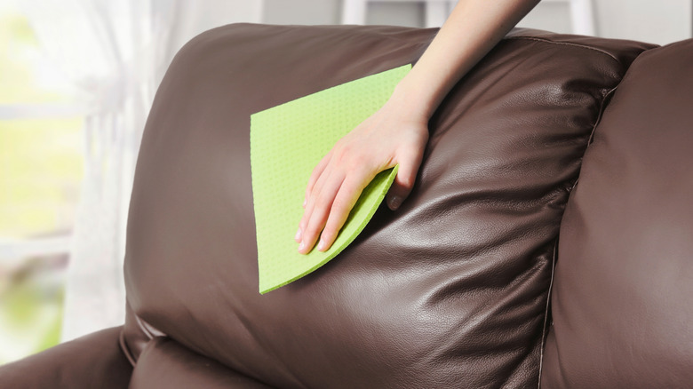 Person cleaning a dark leather sofa with a yellow cloth