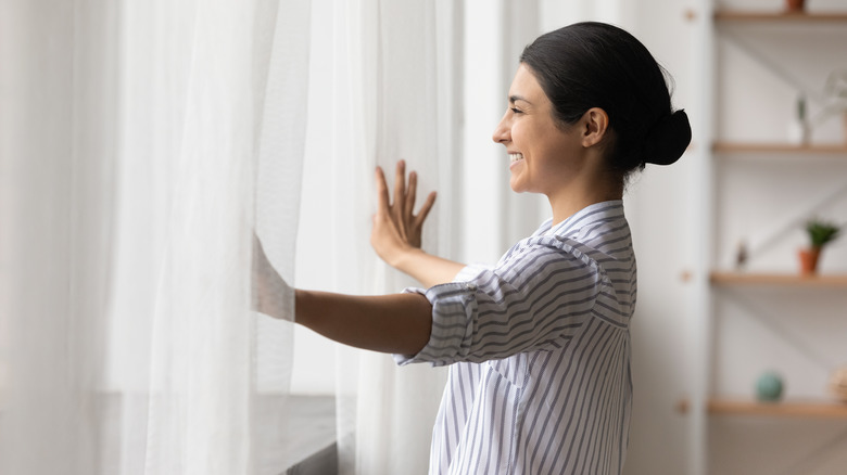 Person smiling, opening window curtains