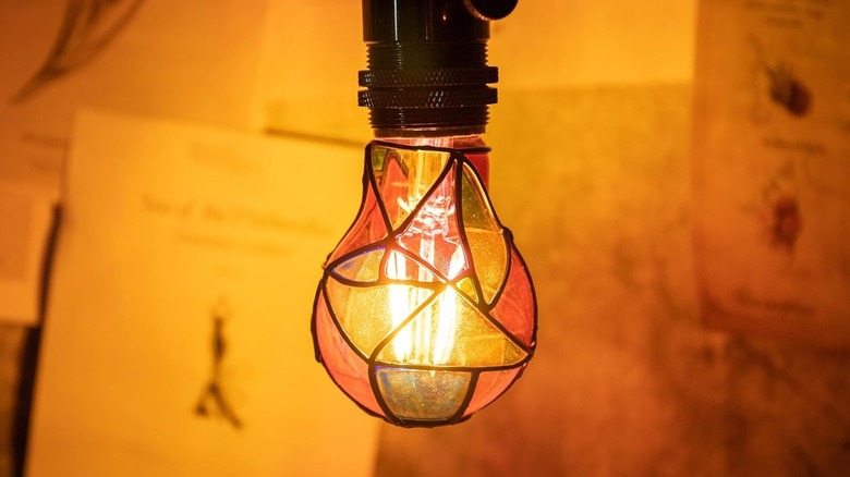 Two stained glass light bulbs: one screwed into a square lamp base and the other into a pendant light socket.