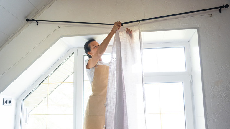 A woman hanging a sheer curtain on a rod