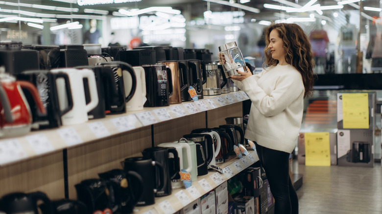A woman in a store looking at different electric teapots