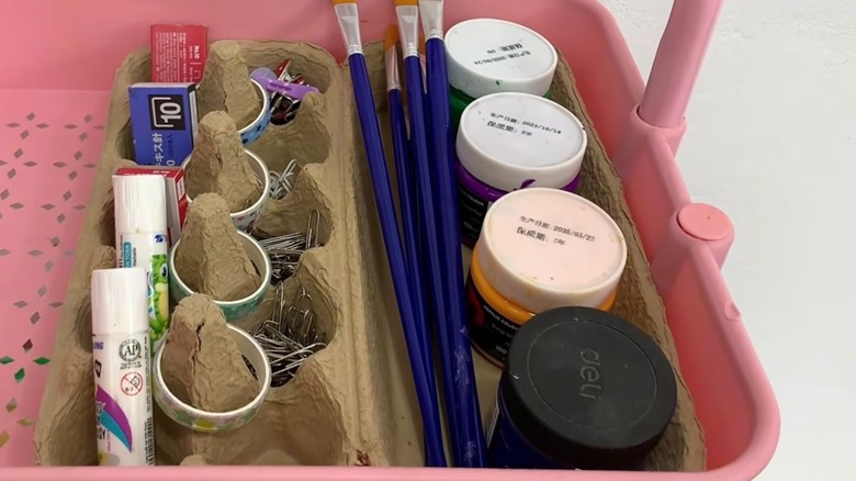 An cardboard egg carton opened out flat and used to store craft supplies in a pink storage cart.