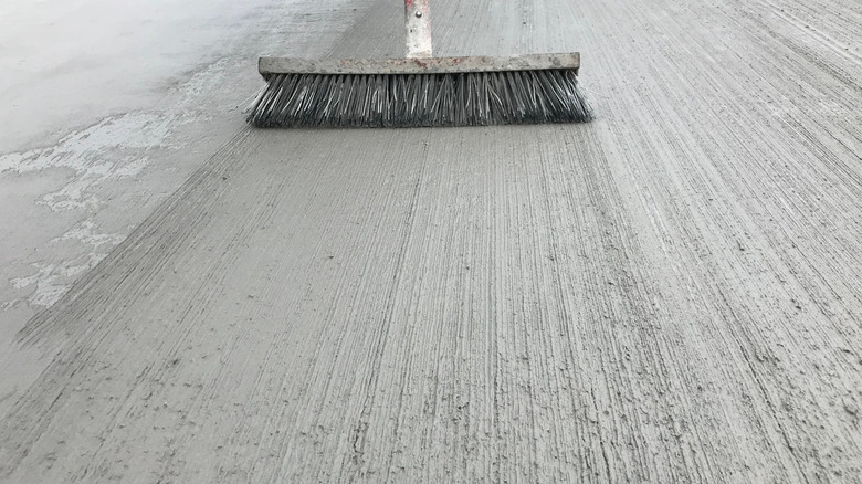 A stiff-bristled broom runs over a freshly laid concrete surface.