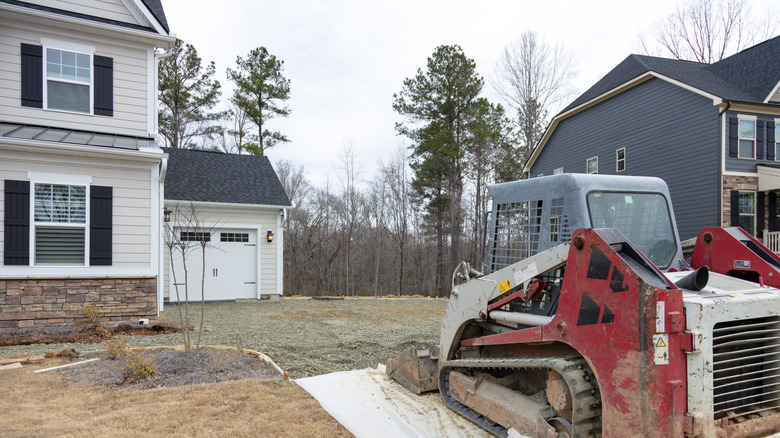 A digger sits in the half-finished driveway of a home in a residential neighborhood.