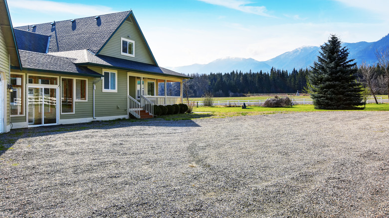 A gravel driveway of a house with mountains in the background