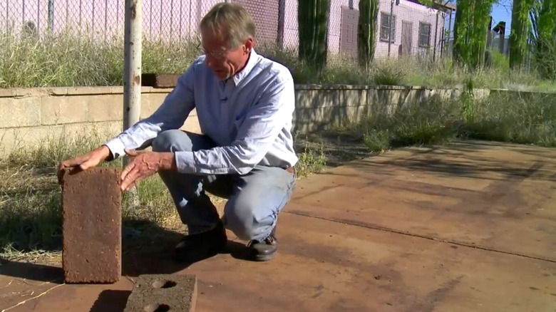 A man crouched down holding a ferrock brick outside.