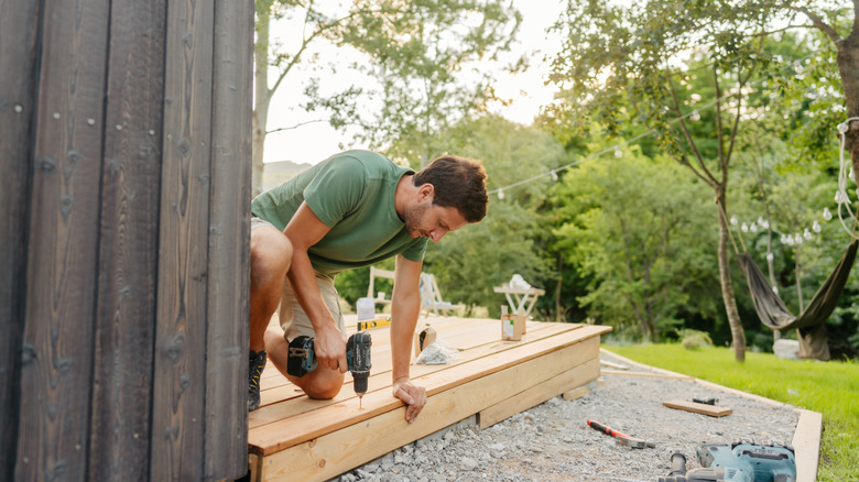 Man drilling screw into wood deck.