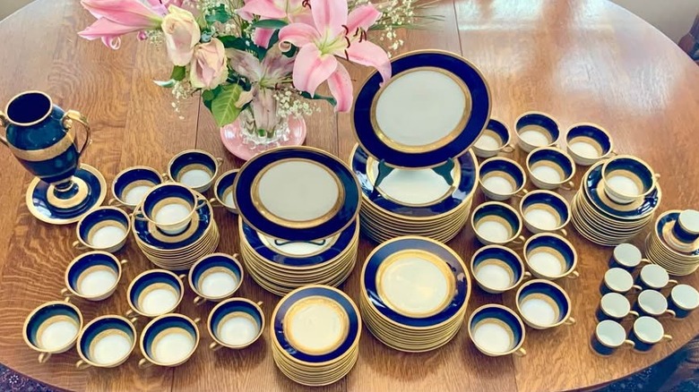 Cobalt blue and gold Limoges set of plates, chargers, and other dishware on a table next to a floral bouquet in a vase