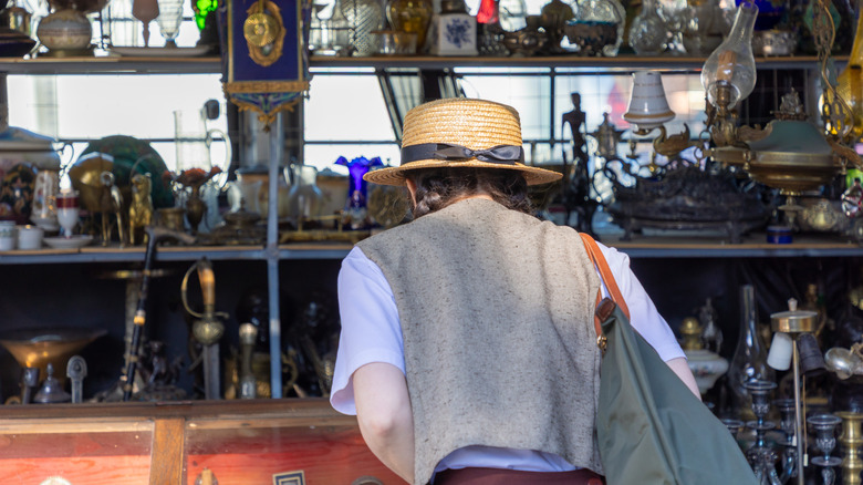 Person wearing a straw hat browses shelves of vintage and antique glassware