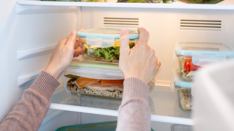Person stacks food storage containers full of leftovers in the fridge.