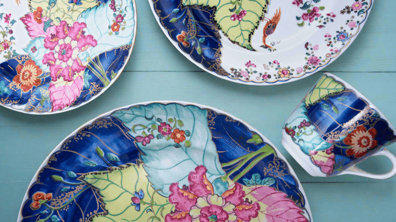 Mottahedeh Tobacco Leaf pattern dinner plates and a tea cup sit on a wooden tabletop painted teal.