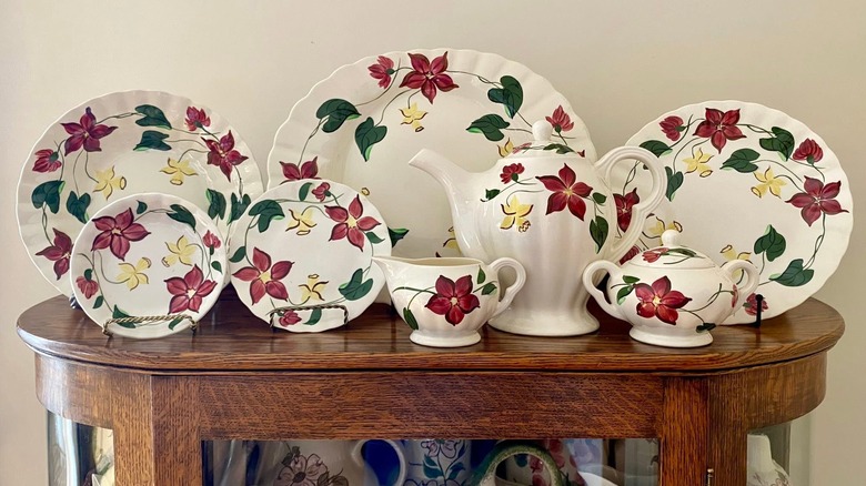 Array of floral Blue Ridge Pottery plates along with a pitcher, gravy boat and sugar bowl, all displayed on top of a hutch