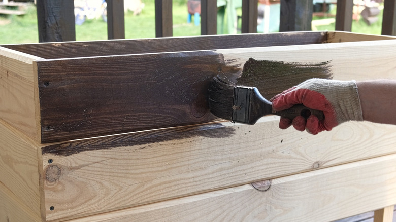 A person using a paint brush to apply stain to a raised bed