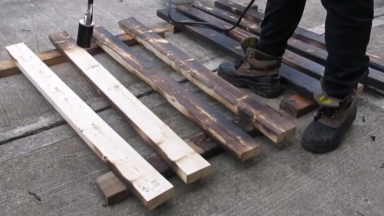 A person using a propane torch to burn individual planks of wood