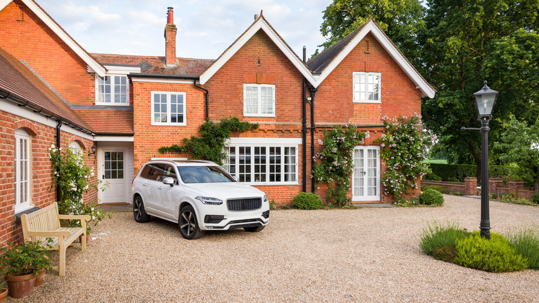 A white SUV is parked on a standard gravel driveway outside of a two-story brick house.