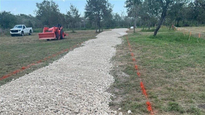 Caliche gravel piled along a marked driveway ready for installation.